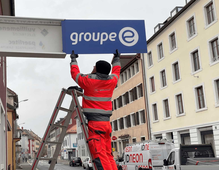 Un collaborateur installe l'enseigne Groupe E sur le mur d'une succursale neuchâteloise