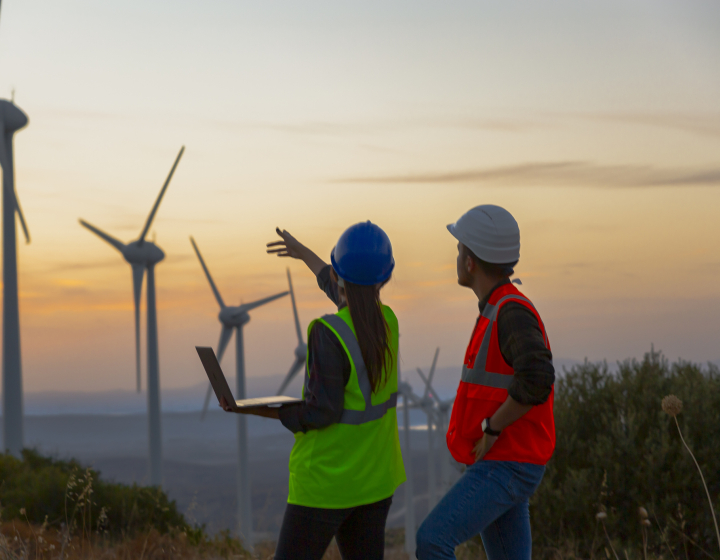 Photo d'un paysage avec des éoliennes et deux personnes analysant les possibilité d'en construire de nouvelle