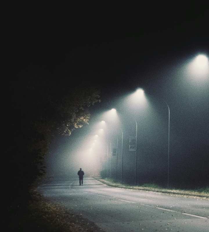 Ein Fußgänger geht allein auf einer Straße, die von Straßenlaternen der Gruppe E beleuchtet wird