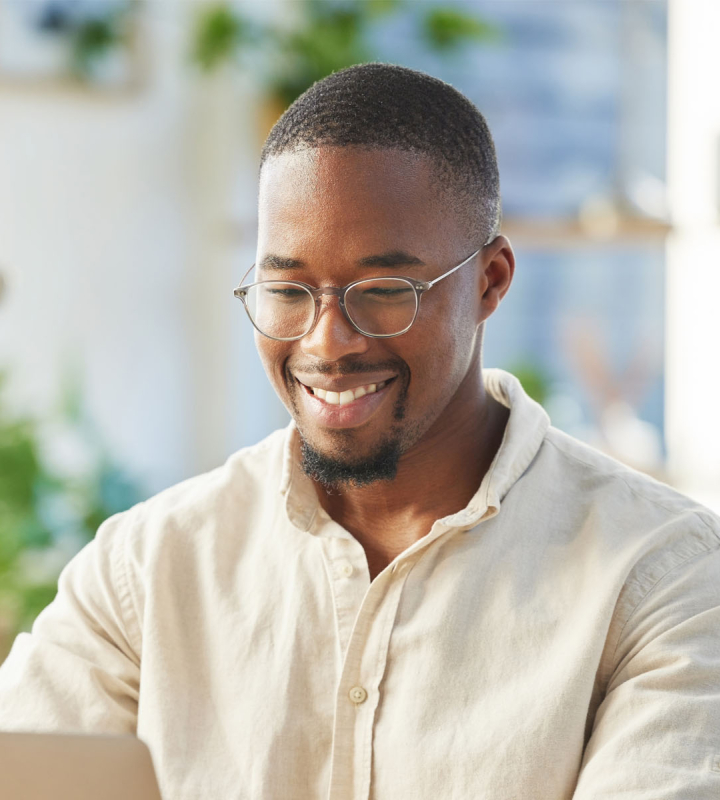 Un homme souriant travaille sur son ordinateur dans un environnement lumineux et accueillant, représentant les avantages de l'offre Électricité Bonus de Groupe E pour les particuliers