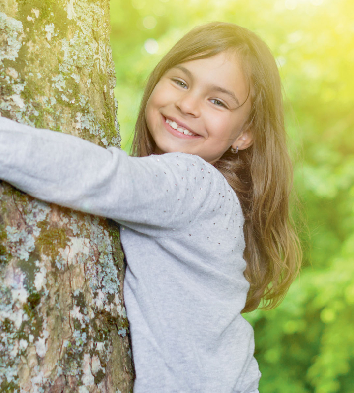 Une jeune fille souriante étreint un arbre, symbolisant l'engagement de Groupe E pour une électricité durable et respectueuse de l'environnement destinée aux particuliers
