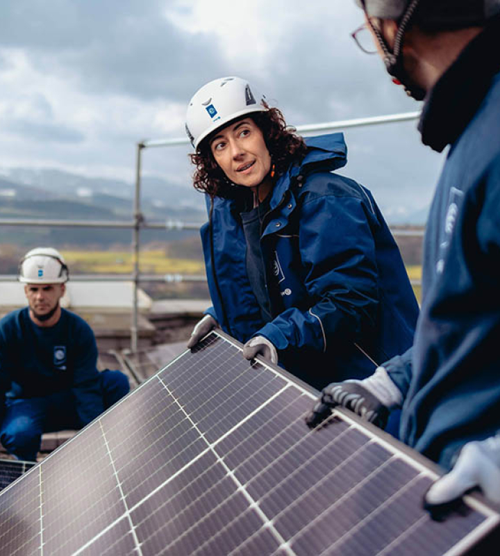 Eine Mitarbeiterin der Groupe E installiert zusammen mit ihren Kollegen Solarzellen auf einem Dach.