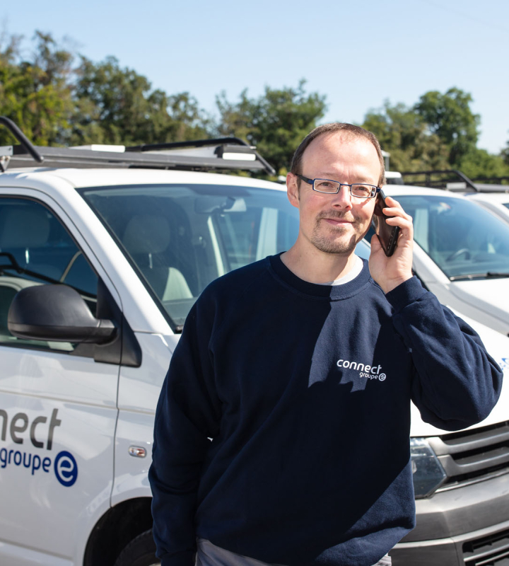 Technicien de Groupe E en communication près d'un véhicule de service, illustrant le service de maintenance pour pompes à chaleur destiné aux professionnels