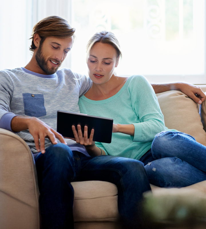 Un couple, installé dans son canapé, est en train d'analyser la courbe de consommation d'énergie du ménage
