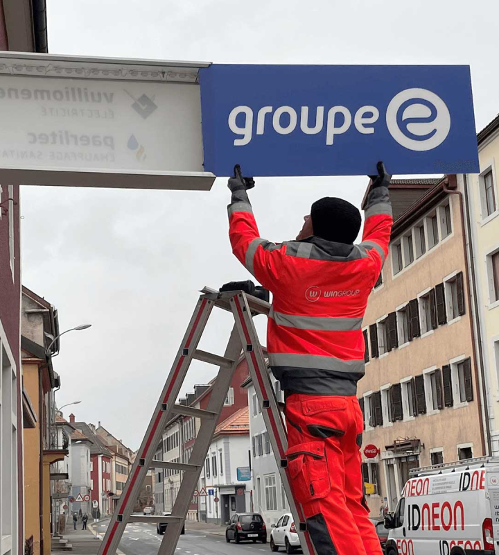 Un collaborateur installe l'enseigne Groupe E sur le mur d'une succursale neuchâteloise.