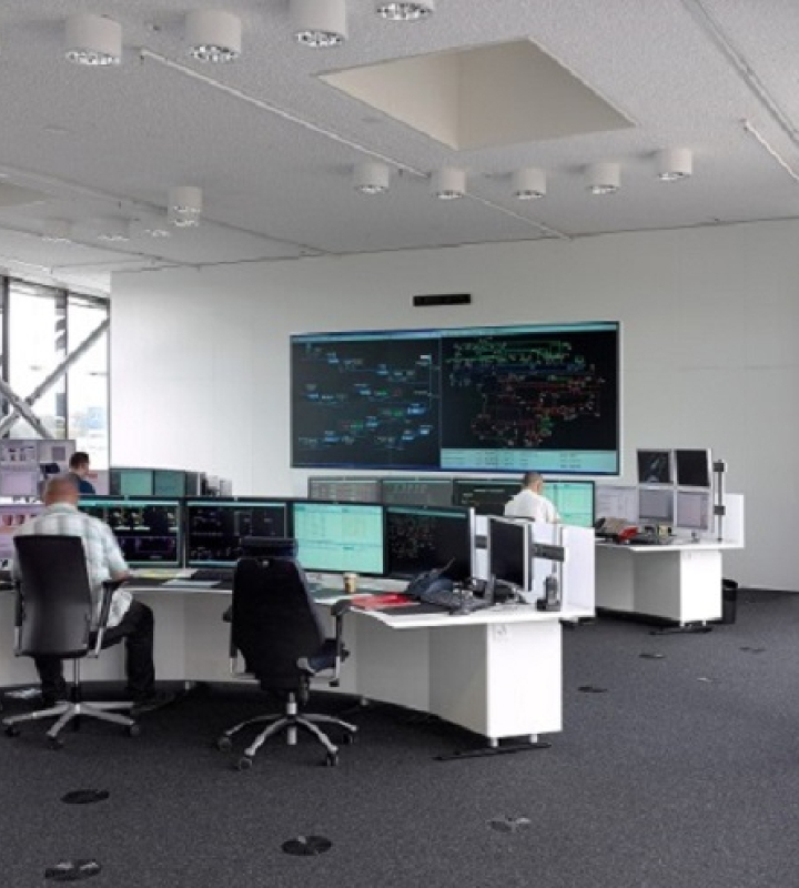 Kontrollzentrum von Groupe E, in dem Operatoren das Energienetz in Echtzeit mithilfe mehrerer Computerbildschirme und einer großen Kontrolltafel an der Wand überwachen. Die moderne und helle Umgebung veranschaulicht das Engagement von Groupe E in der fortschrittlichen Energiemanagement und der Überwachung seiner Infrastruktur.