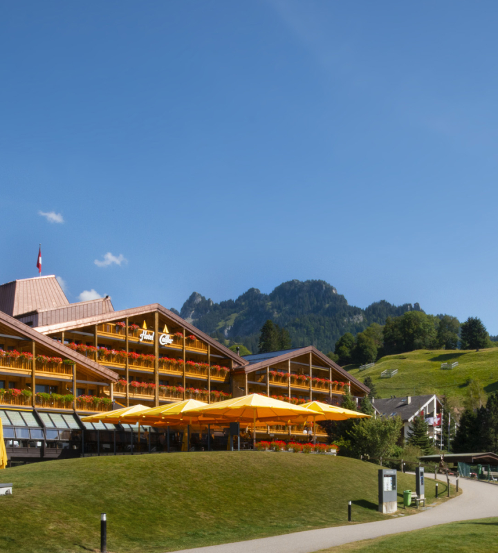 Aussenansicht eines Hotels, umgeben von Bergen und Grünflächen, in einer sonnigen natürlichen Umgebung, das möglicherweise die Energieinstallationen und den Komfort symbolisiert, den Groupe E in einem ähnlichen Umfeld bieten könnte.