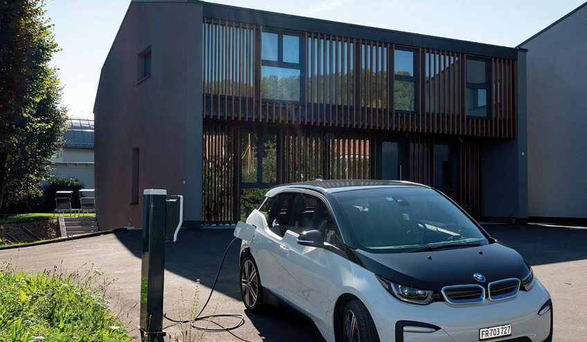 Une voiture électrique en charge devant une villa privée grâce à une borne installée par Groupe E