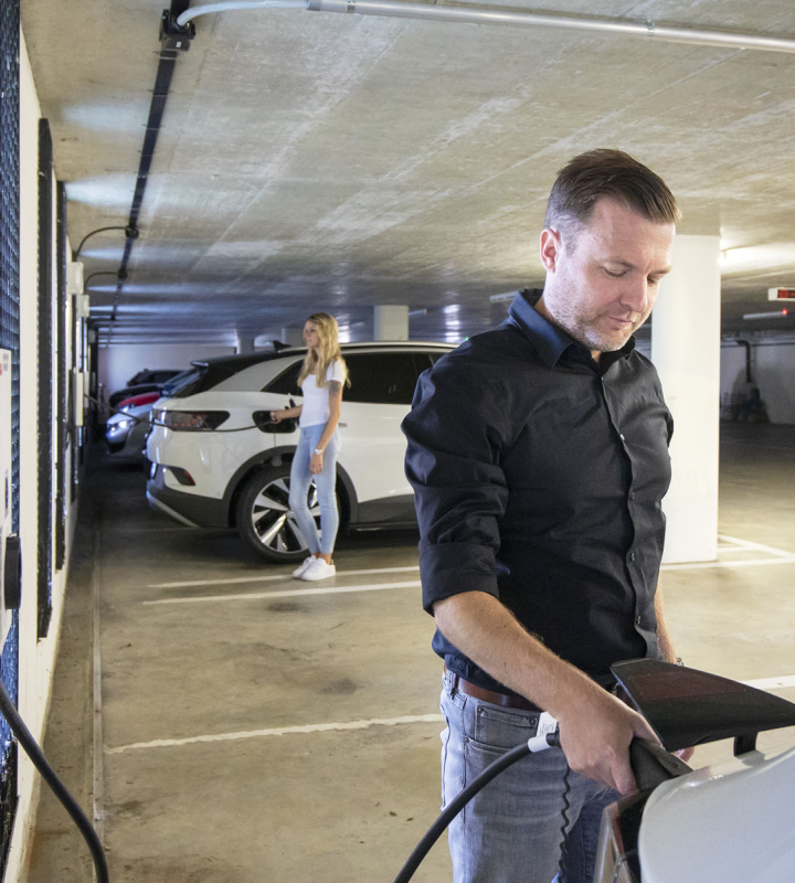 Homme rechargeant une voiture électrique dans un parking illustrant les solutions d'achat et de location de bornes électriques proposées par Groupe E pour les professionnels