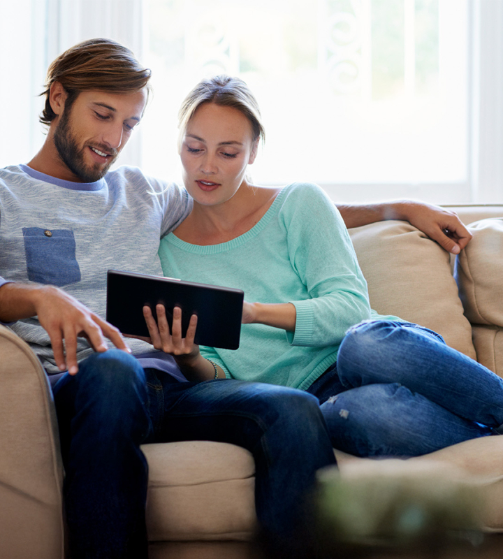 Un couple, installé dans son canapé, est en train d'analyser la courbe de consommation d'énergie du ménage