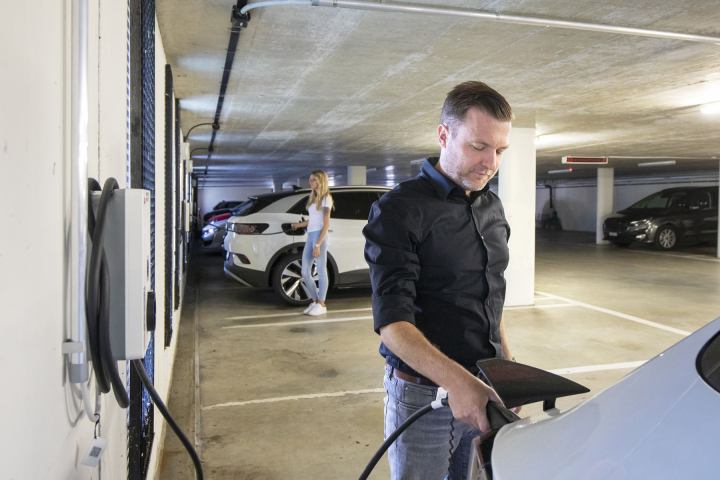 Homme rechargeant une voiture électrique dans un parking illustrant les solutions d'achat et de location de bornes électriques proposées par Groupe E pour les professionnels