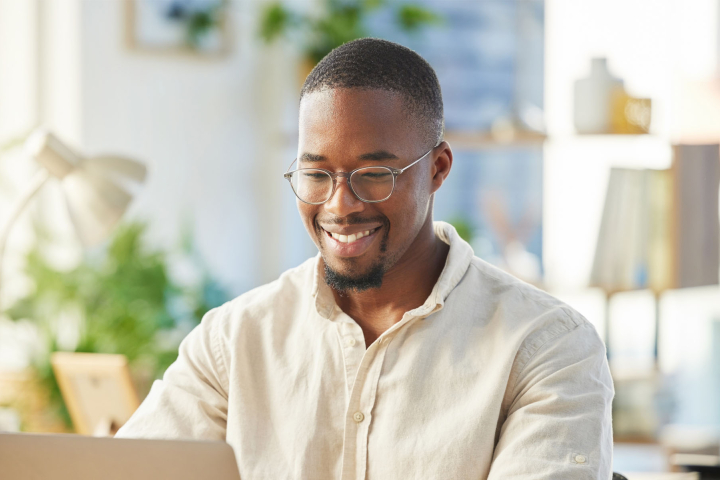 Un homme souriant travaille sur son ordinateur dans un environnement lumineux et accueillant, représentant les avantages de l'offre Électricité Bonus de Groupe E pour les particuliers