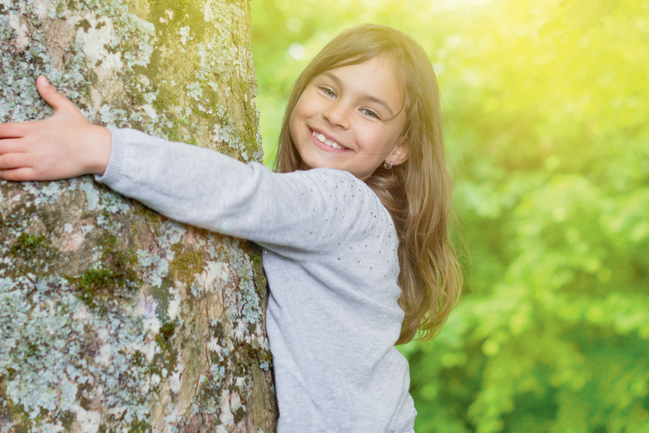 Une jeune fille souriante étreint un arbre, symbolisant l'engagement de Groupe E pour une électricité durable et respectueuse de l'environnement destinée aux particuliers