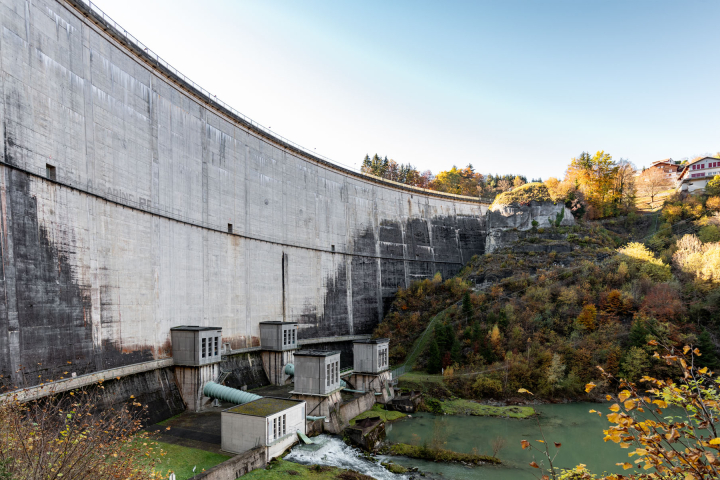 Ansicht eines Wasserkraftwerksdamms, umgeben von herbstlicher Natur, der die Expertise von Groupe E im Bereich Wasserkraft und seine spezialisierten Schulungen veranschaulicht