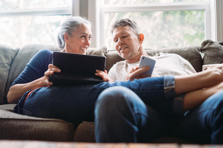 Un couple détendu à la maison, consultant une tablette et un smartphone, illustrant la simplicité et l'accessibilité des solutions de facturation de chauffage à distance proposées par Groupe E pour les clients privés