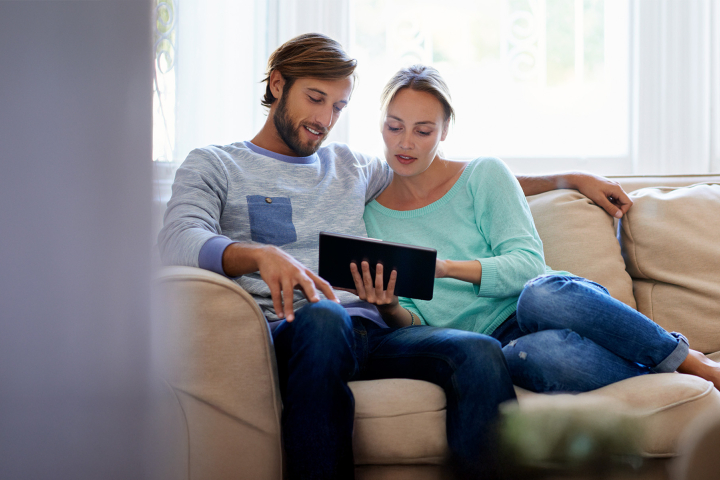 Un couple, installé dans son canapé, est en train d'analyser la courbe de consommation d'énergie du ménage